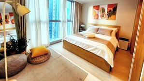 A modern hotel room with a large bed, a bedside table, a lamp, and a view of the city.