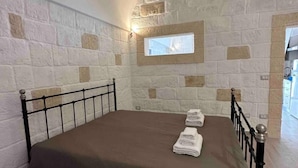 A bedroom with a stone wall, a bed with a brown bedspread, and a small window.