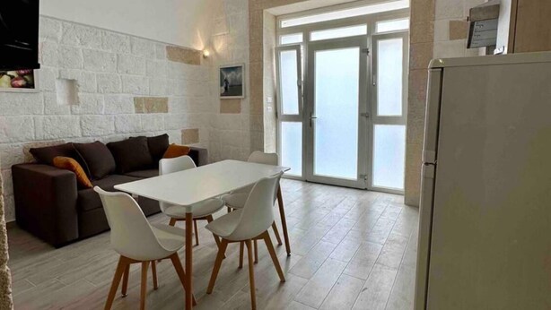 A spacious living area with a white table and chairs, a dark sofa, and a large window with a view.