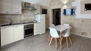 A modern kitchen with a stone wall, a dining area with white chairs, and a built-in oven.