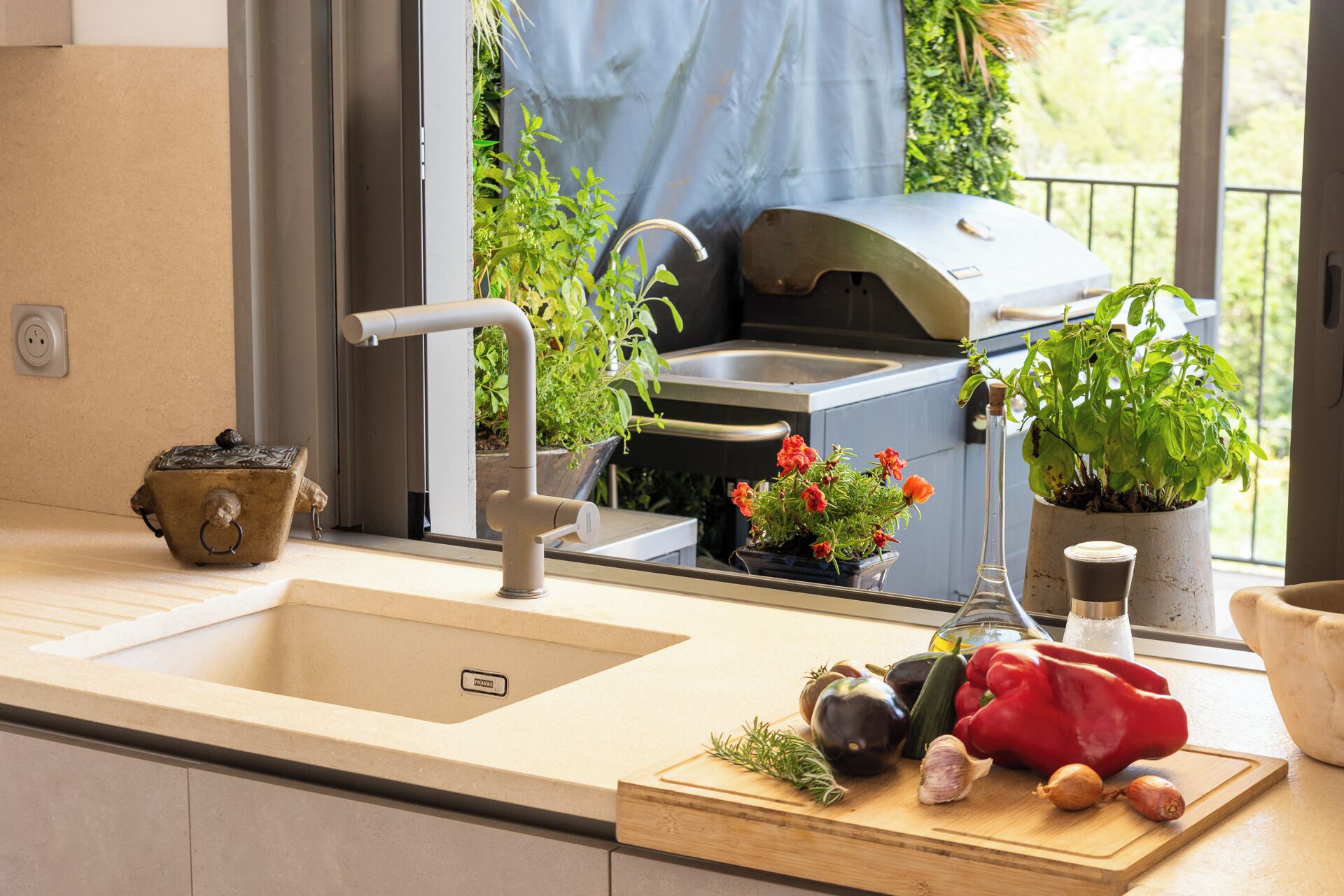 Une cuisine équipée d’un évier, d’un barbecue intégré et de divers légumes frais disposés sur le plan de travail.