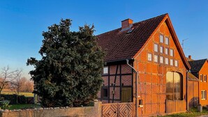 Et traditionelt bindingsværkshus med skråt tag, et stort træ foran og en træport.