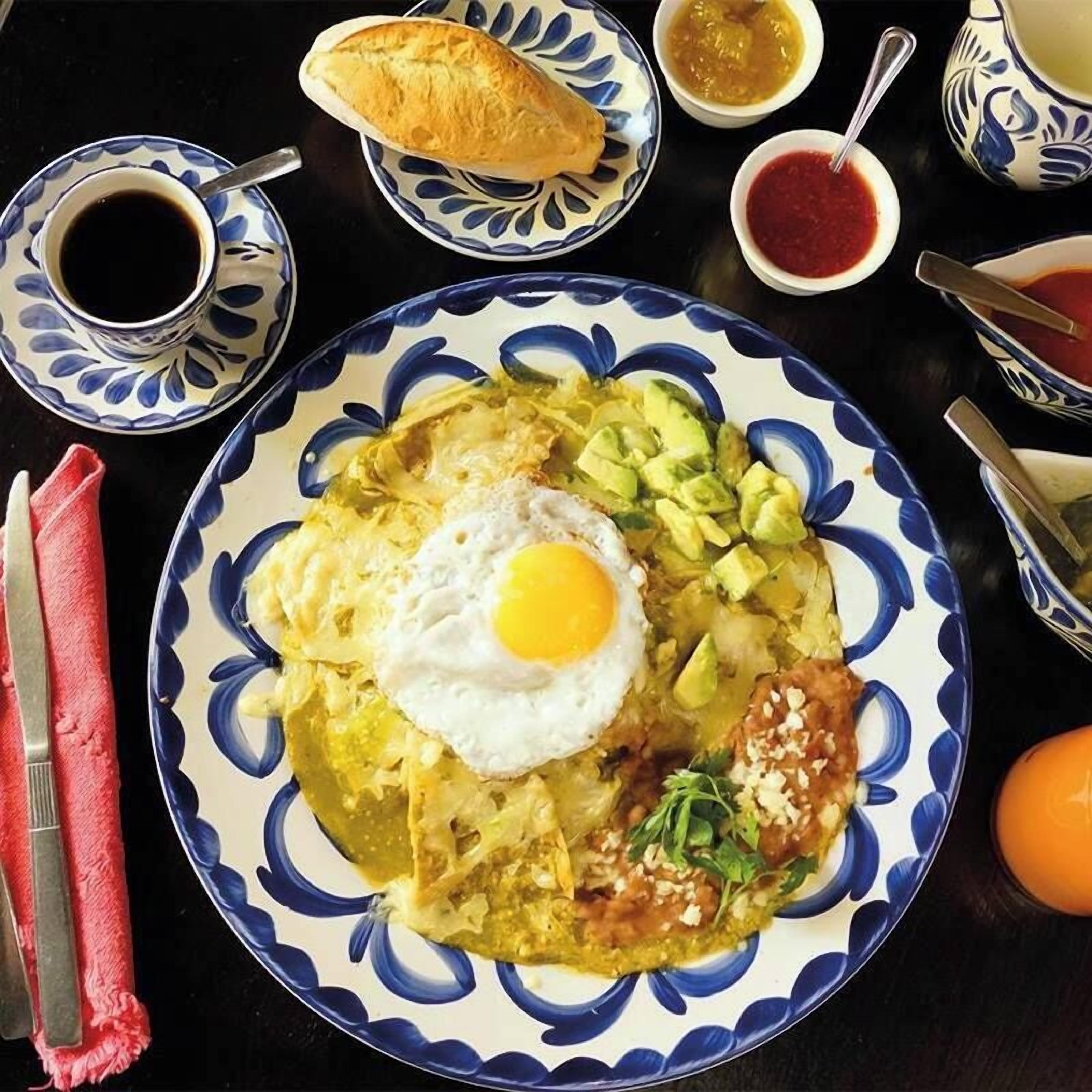 A plate of food with a fried egg, avocado, and other toppings, accompanied by bread and condiments on a table.