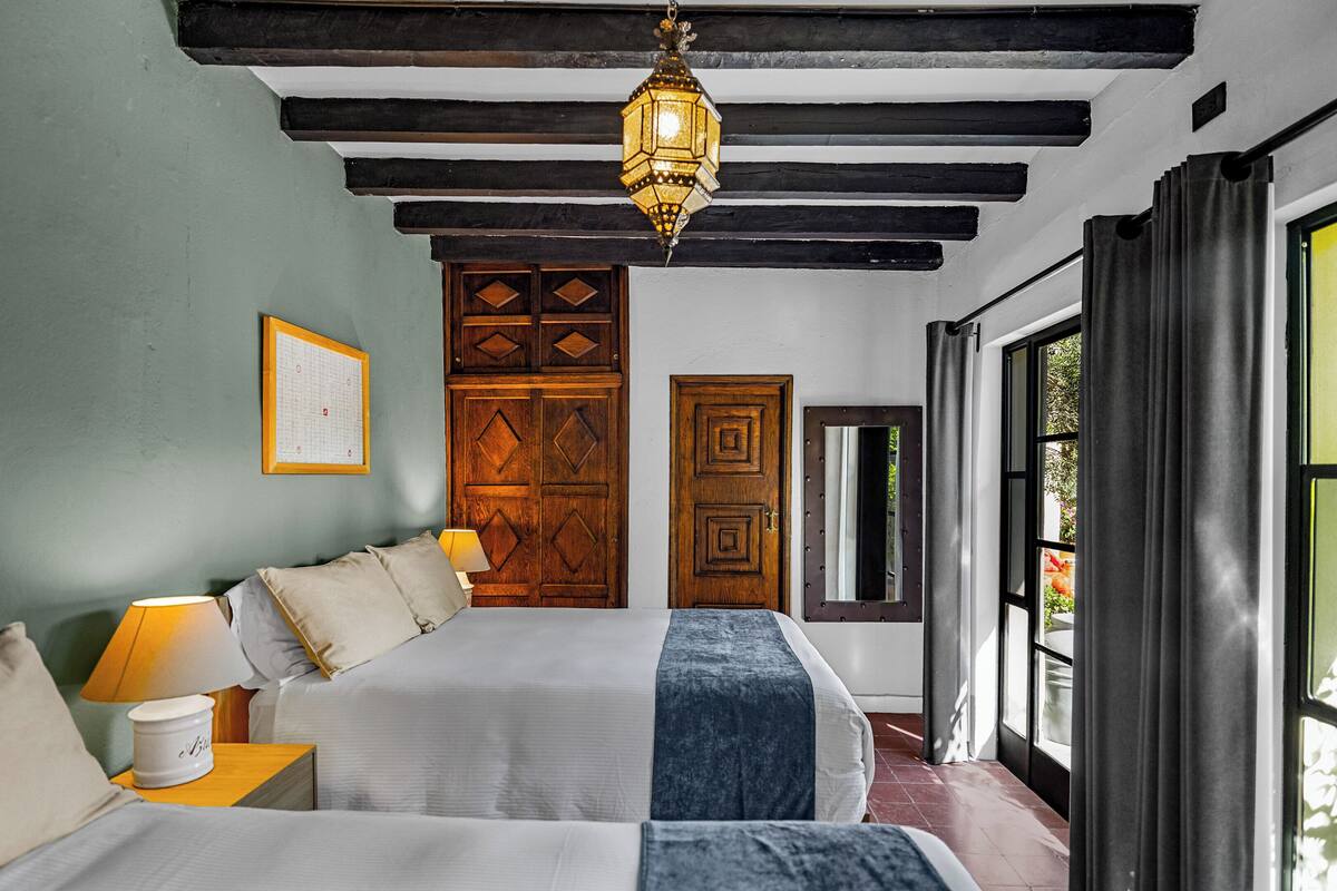 A bedroom with a bed, a nightstand, a lamp, a wooden door, and a window.
