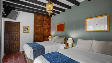A room with two beds, a wooden door, a wall-mounted lamp, and a framed chart on the wall.