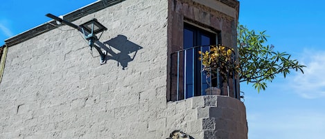 Um edifício com fachada desgastada, um poste de luz, uma janela com vaso de flores e uma placa de sinalização.