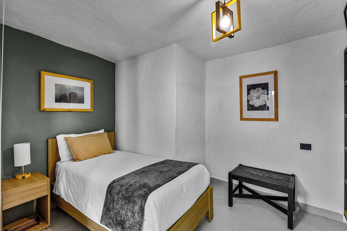 A neatly arranged bedroom with a bed, bedside table, bench, and two framed pictures on the walls.