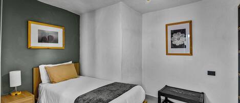 A neatly arranged bedroom with a bed, bedside table, bench, and two framed pictures on the walls.