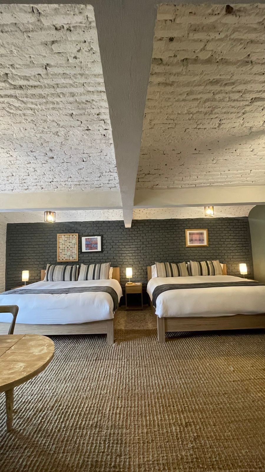 Habitación de hotel con dos camas, una pared de ladrillo y un techo texturizado.