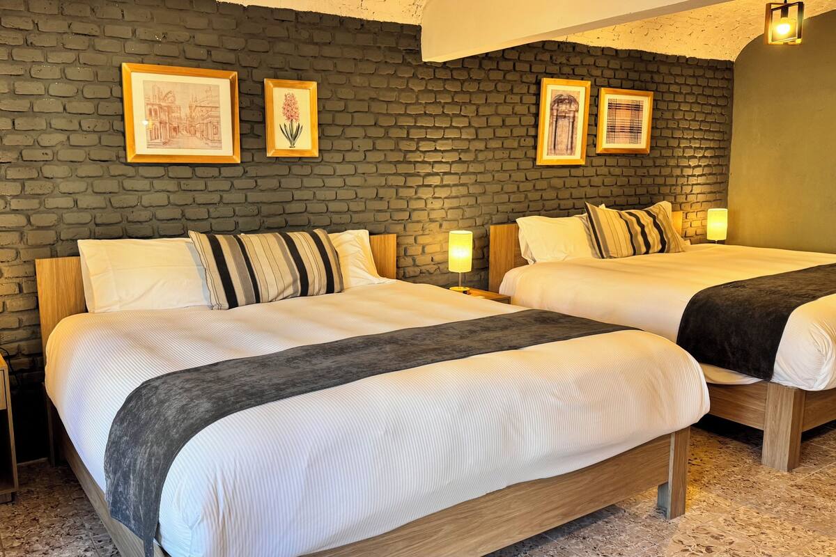 A hotel room with two beds, a brick wall, and framed artwork.