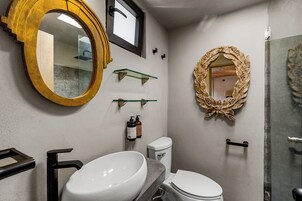 Un baño con un espejo ovalado grande, un lavamanos blanco, un inodoro y una zona de ducha.