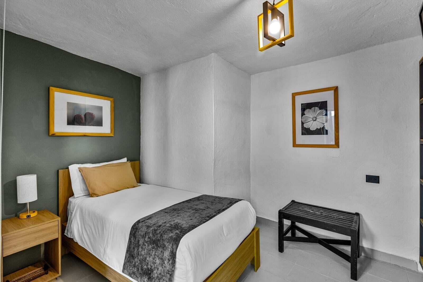 A bedroom with a bed, bedside table, lamp, and two framed pictures on the wall.