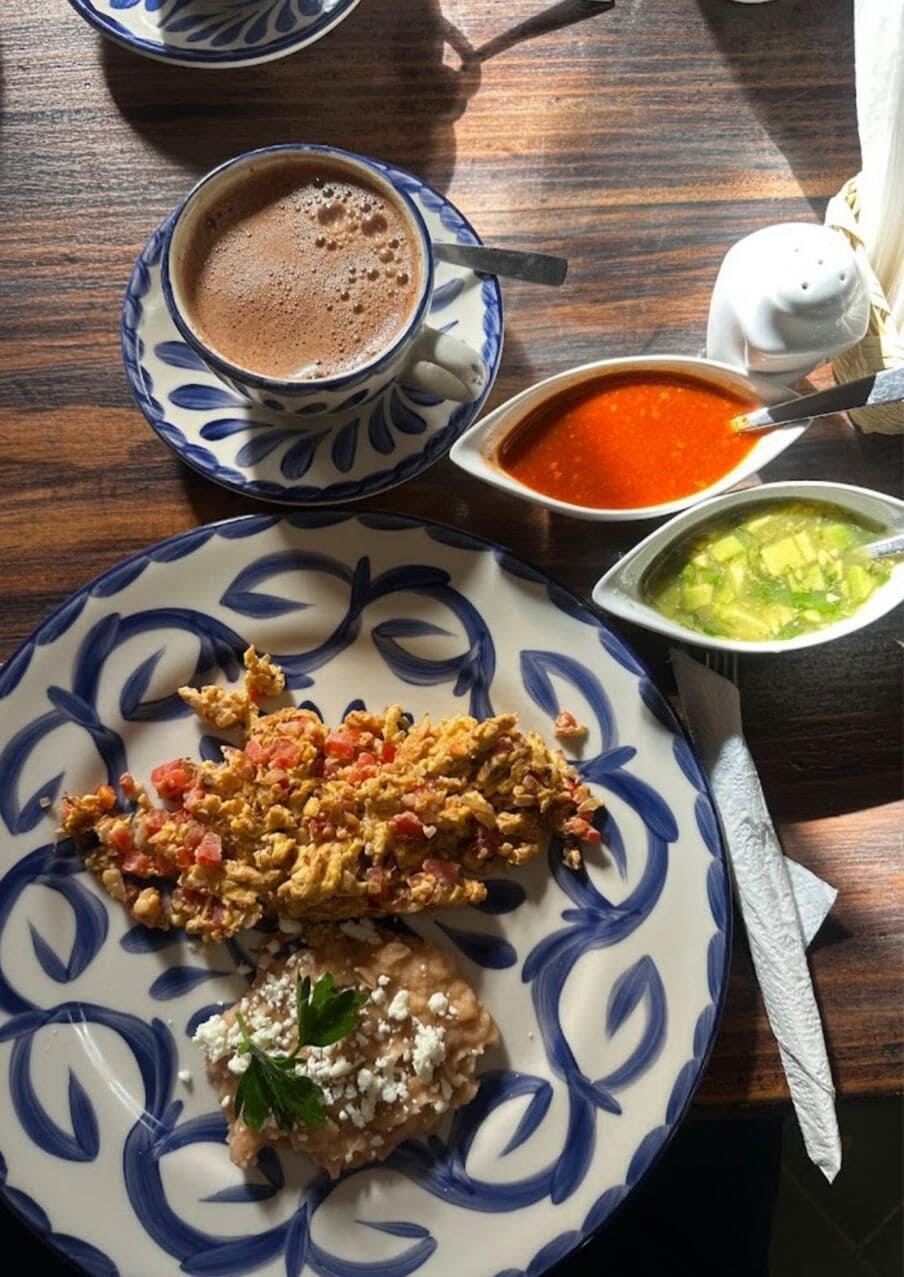 A table with a plate of scrambled eggs, a cup of coffee, and two bowls of soup.
