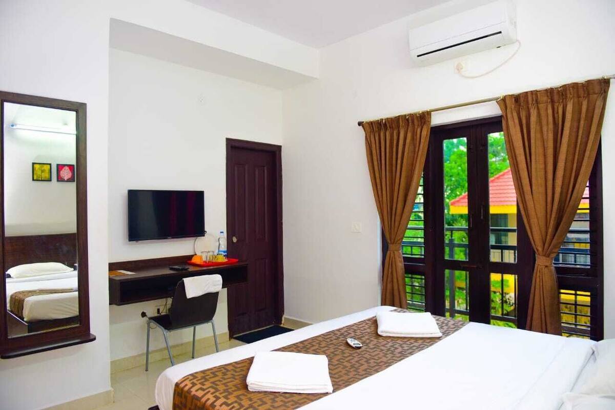 A hotel room with a bed, a desk, a chair, a TV, and a window with curtains.
