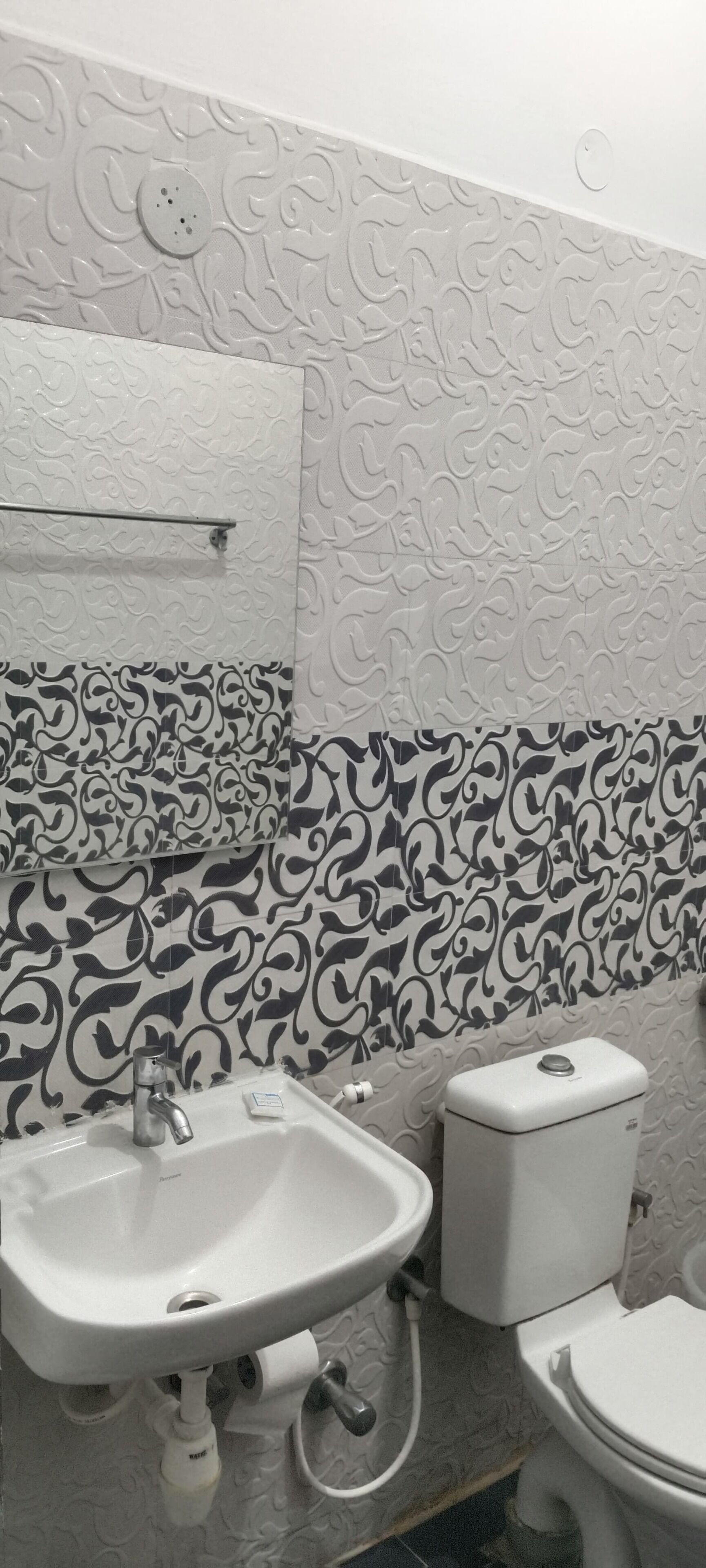 Un baño con lavamanos blanco, inodoro y azulejos de pared estampados.