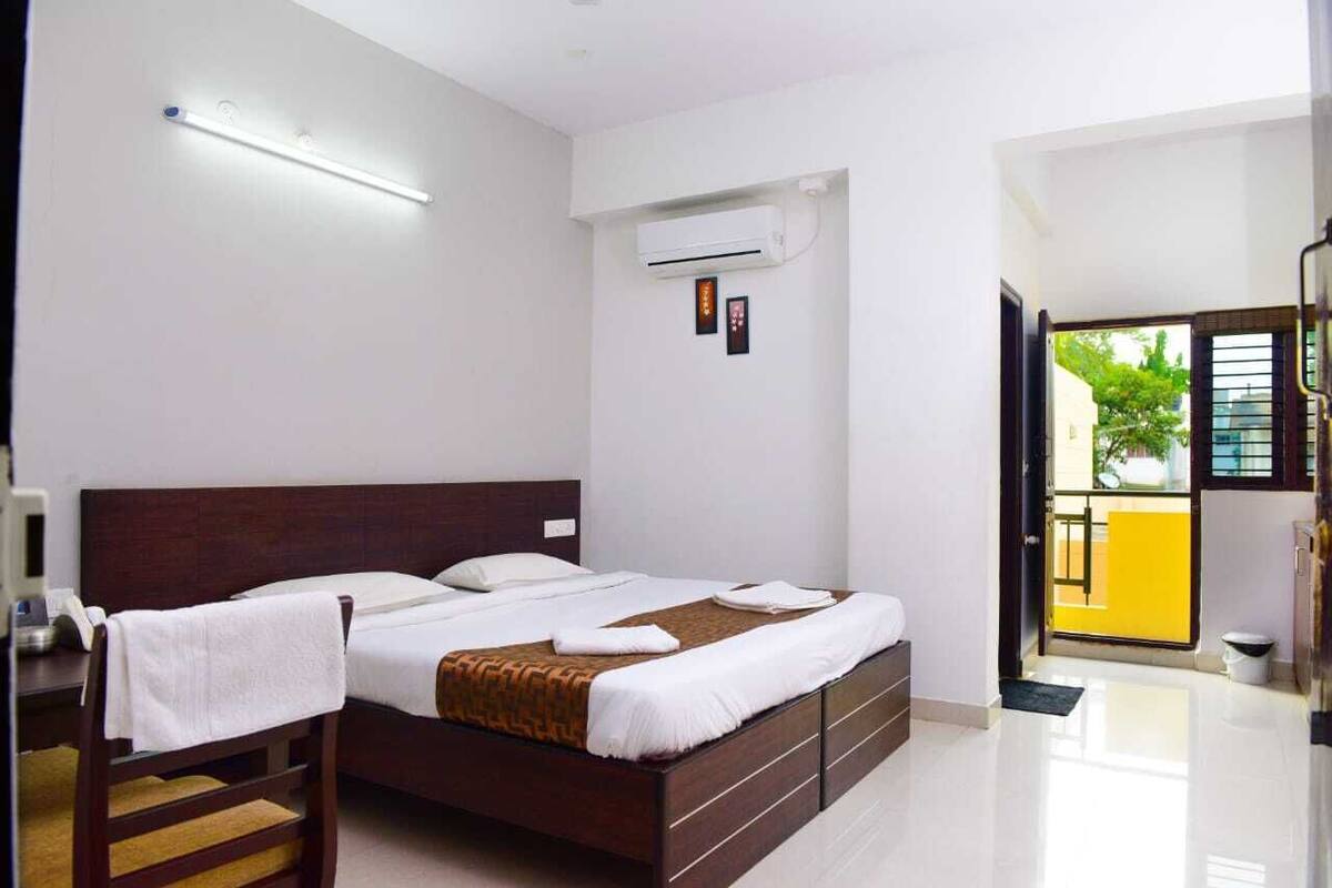 A hotel room with a bed, bedside tables, an air conditioning unit, and a view of the outside.
