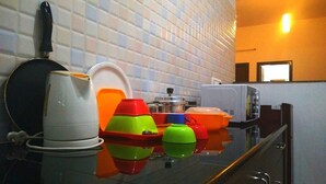 A kitchen with a tiled backsplash, a stove, and various colorful kitchenware on the counter. - VARSHA ENCLAVE TRINITY HOUSE (Mysore)