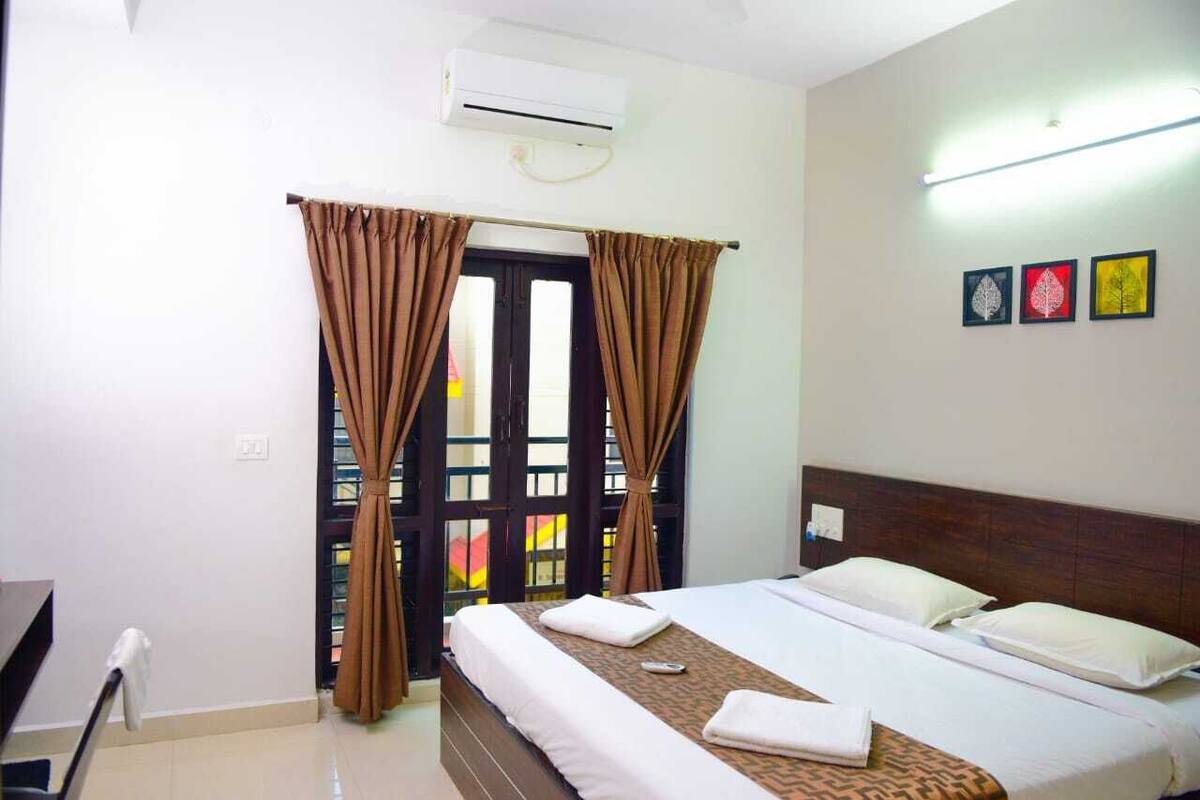 A hotel room with a bed, curtains, an air conditioner, and a wall with three framed pictures.
