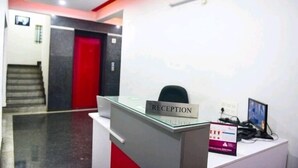 A reception area with a reception desk, a red door, and a staircase in the background. - VARSHA ENCLAVE TRINITY HOUSE (Mysore)