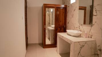 Un baño con puerta de madera, lavamanos blanco y pared con azulejos de mármol.