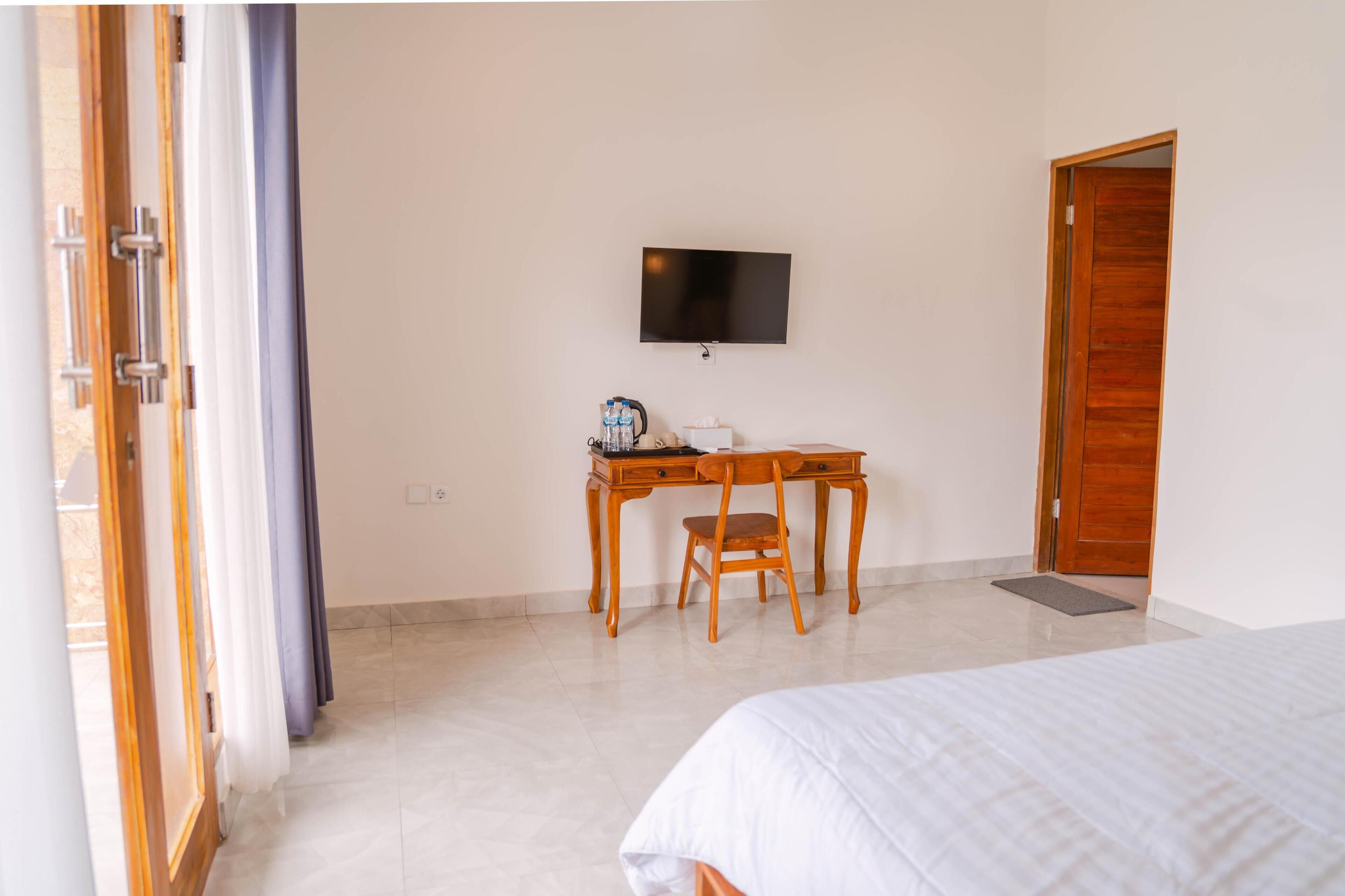 A hotel room with a bed, a desk with a chair, a television on the wall, and a wooden door.
