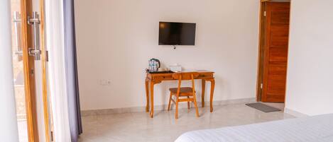 A hotel room with a bed, a desk with a chair, a television on the wall, and a wooden door.