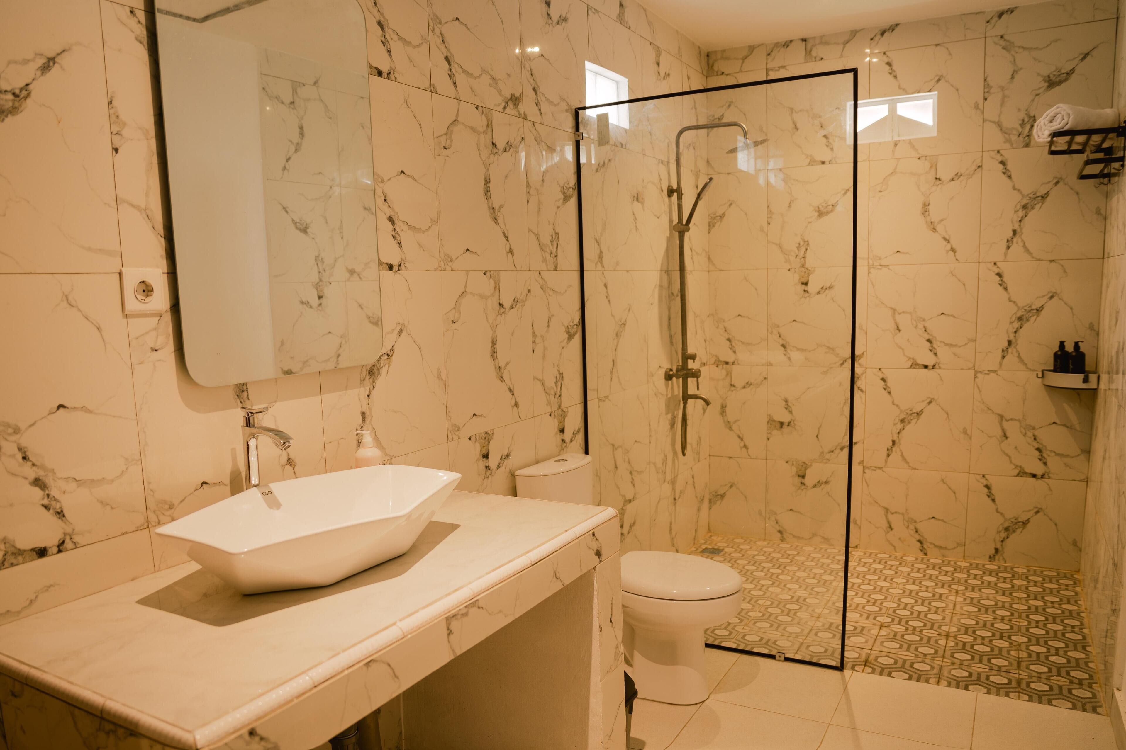 A bathroom with a marble wall, a glass shower enclosure, a white sink, and a toilet.