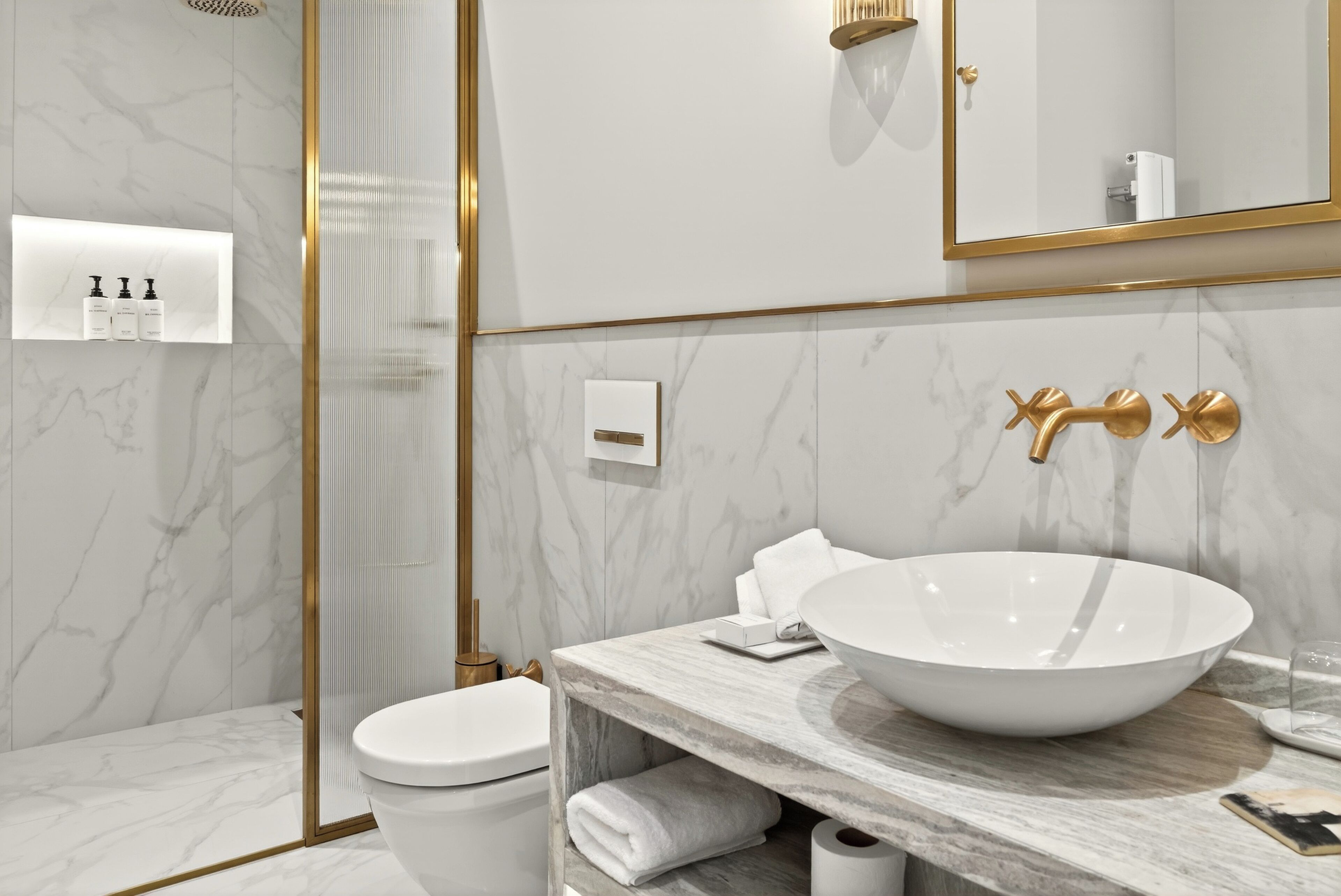 Een moderne badkamer met een wit toilet, een groot witte wastafel en een spiegel met gouden lijst.