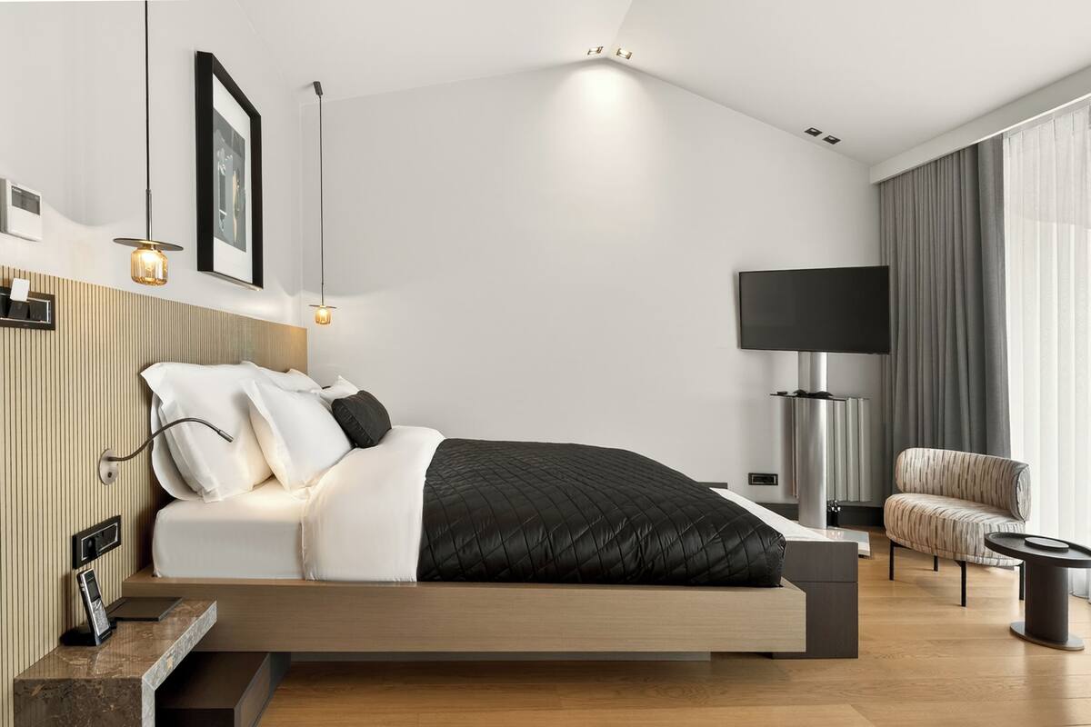 A modern bedroom with a bed, bedside table, lamp, TV, and a chair.