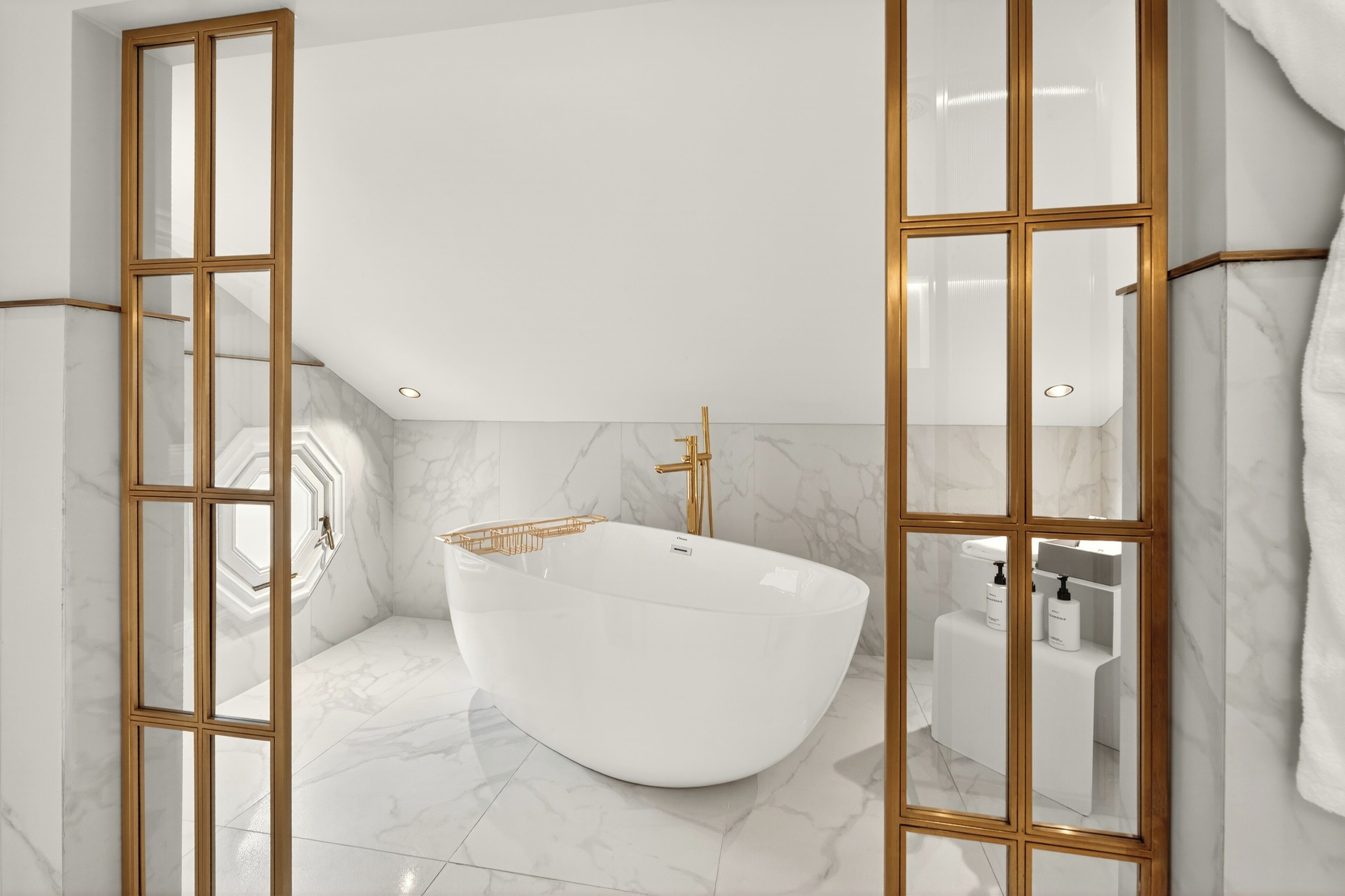 Ein modernes Badezimmer mit freistehender Badewanne, Marmorböden und Spiegeln mit goldfarbenen Rahmen.