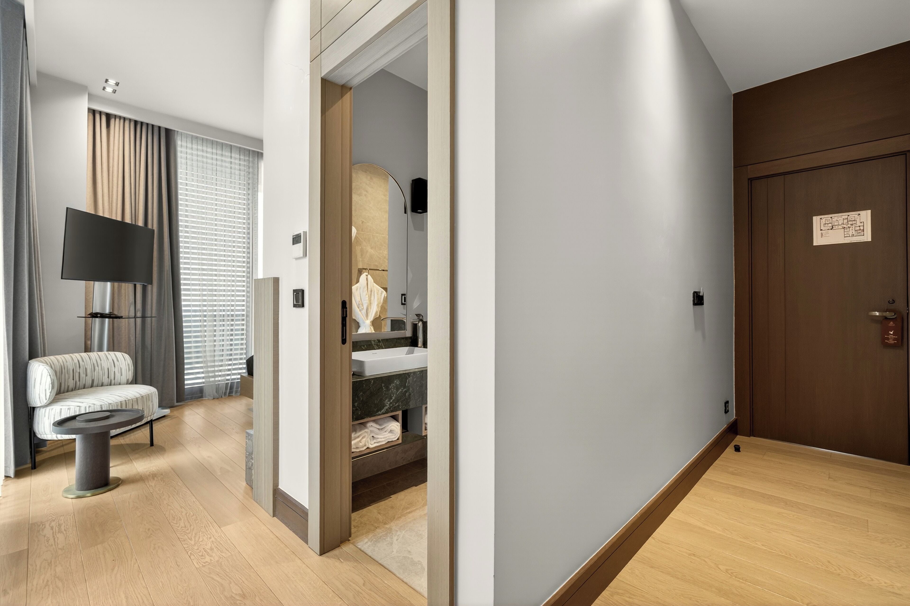A hotel room with a sofa, a TV, a bathroom with a sink and mirror, and a wooden door with a map.