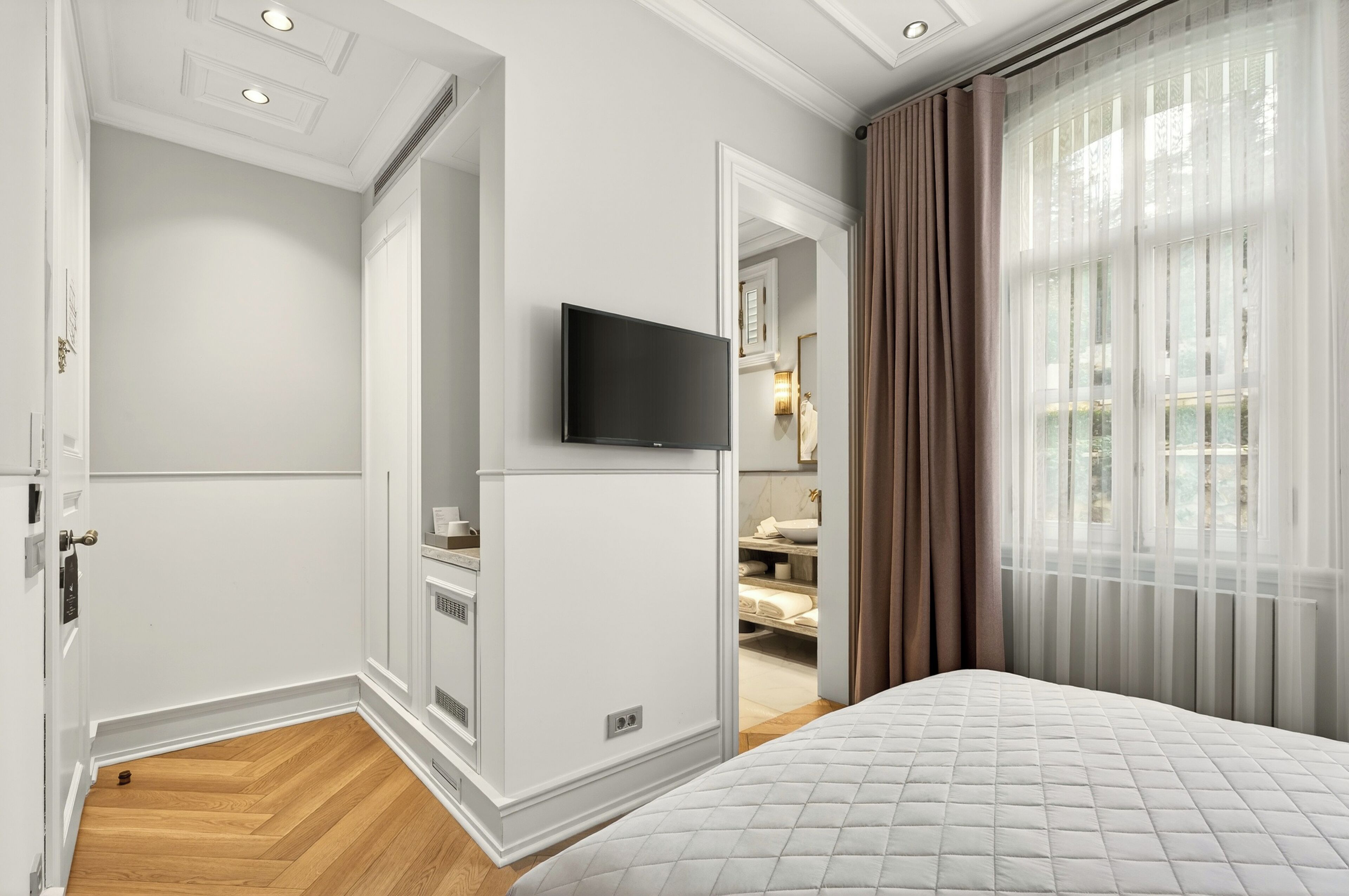 A hotel room with a bed, a television, a wardrobe, and a bathroom visible through an open door.