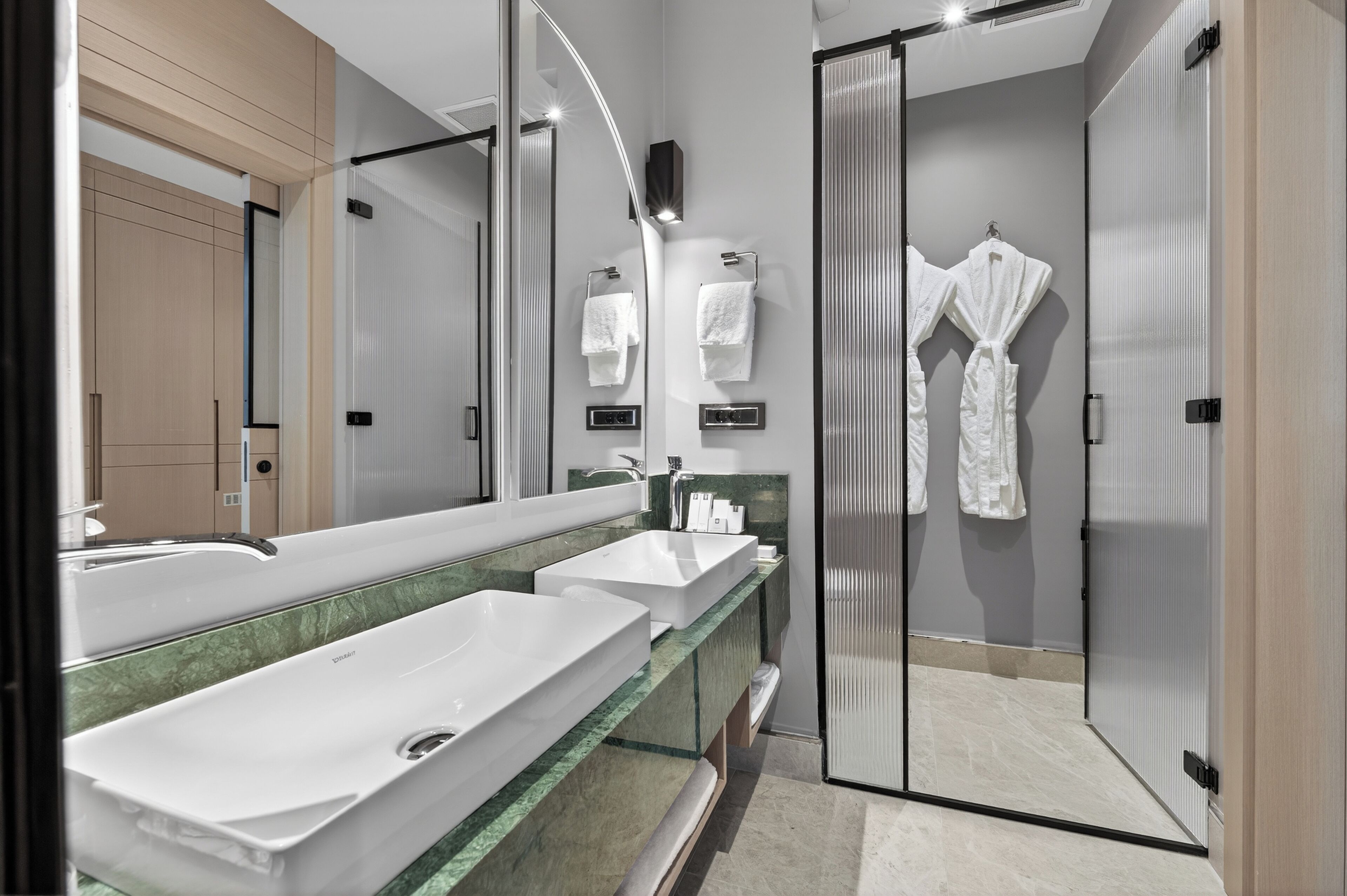 Un baño moderno con tres lavamanos, un espejo grande y una cabina de ducha de vidrio.