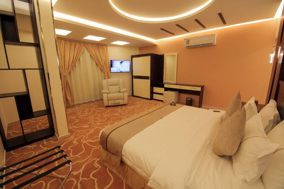 A hotel room with a large bed, a chair, a desk, a television, and a mirror.