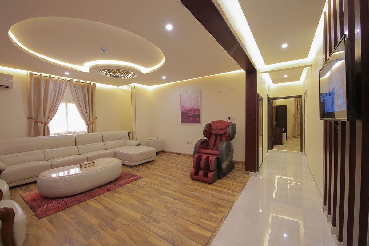 A modern living room with a sofa set, a massage chair, and a flat-screen TV.