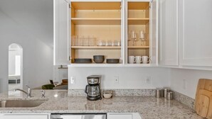 A modern kitchen with white cabinetry, a granite countertop, and a coffee maker.