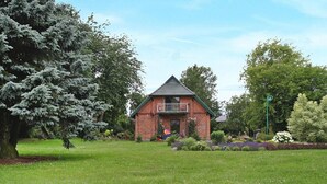 A brick house with a balcony, surrounded by a well-maintained lawn and various trees.