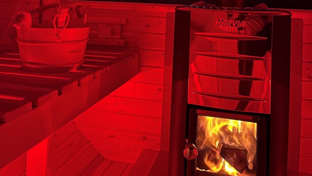 A cozy cabin interior with a wood-burning stove, a bucket, and a view of the night sky.