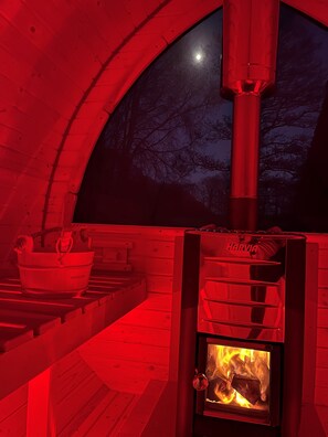 A cozy cabin interior with a wood-burning stove, a bucket, and a view of the night sky.