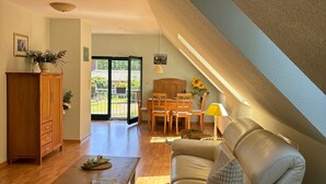 A spacious living room with a high ceiling, a dining area, and a view through a glass door.