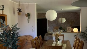 A dining area with a wooden table, chairs, hanging plants, and a ceiling light fixture.