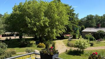 Un balcone con ringhiera metallica che si affaccia su un giardino con diverse piante e un albero grande.