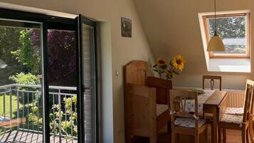 Habitació amb zona de menjador, finestra que ofereix vista a vegetació i balcó amb porta de vidre.