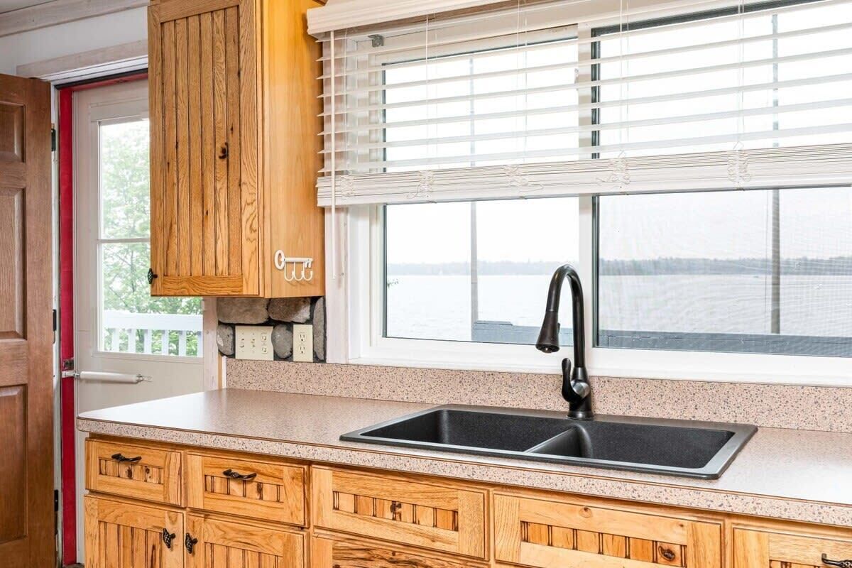 A kitchen with wooden cabinets, a granite countertop, a black sink, and a window with blinds.