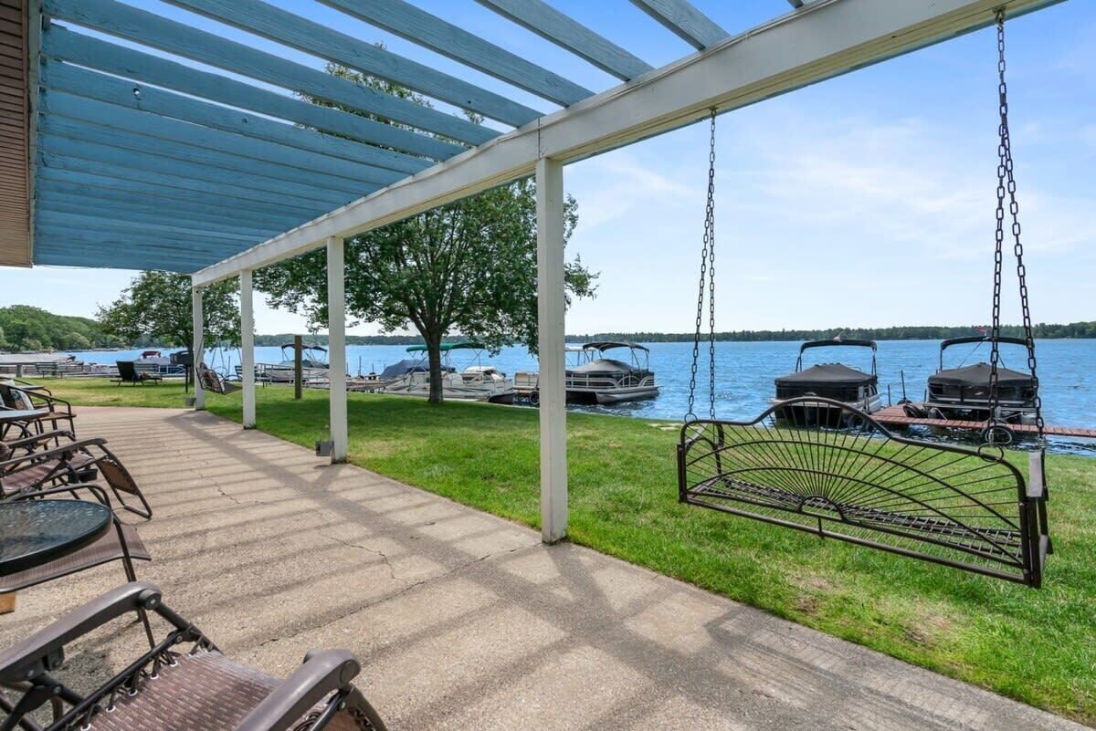 A covered patio with outdoor seating, a swing, and boats on the water in the background.