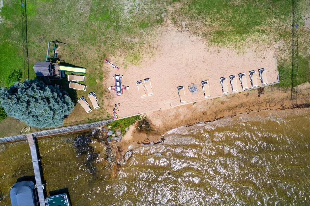 Luchtbeeld van een pand aan de rivier met een steiger, een rij strandstoelen en een klein bootje.