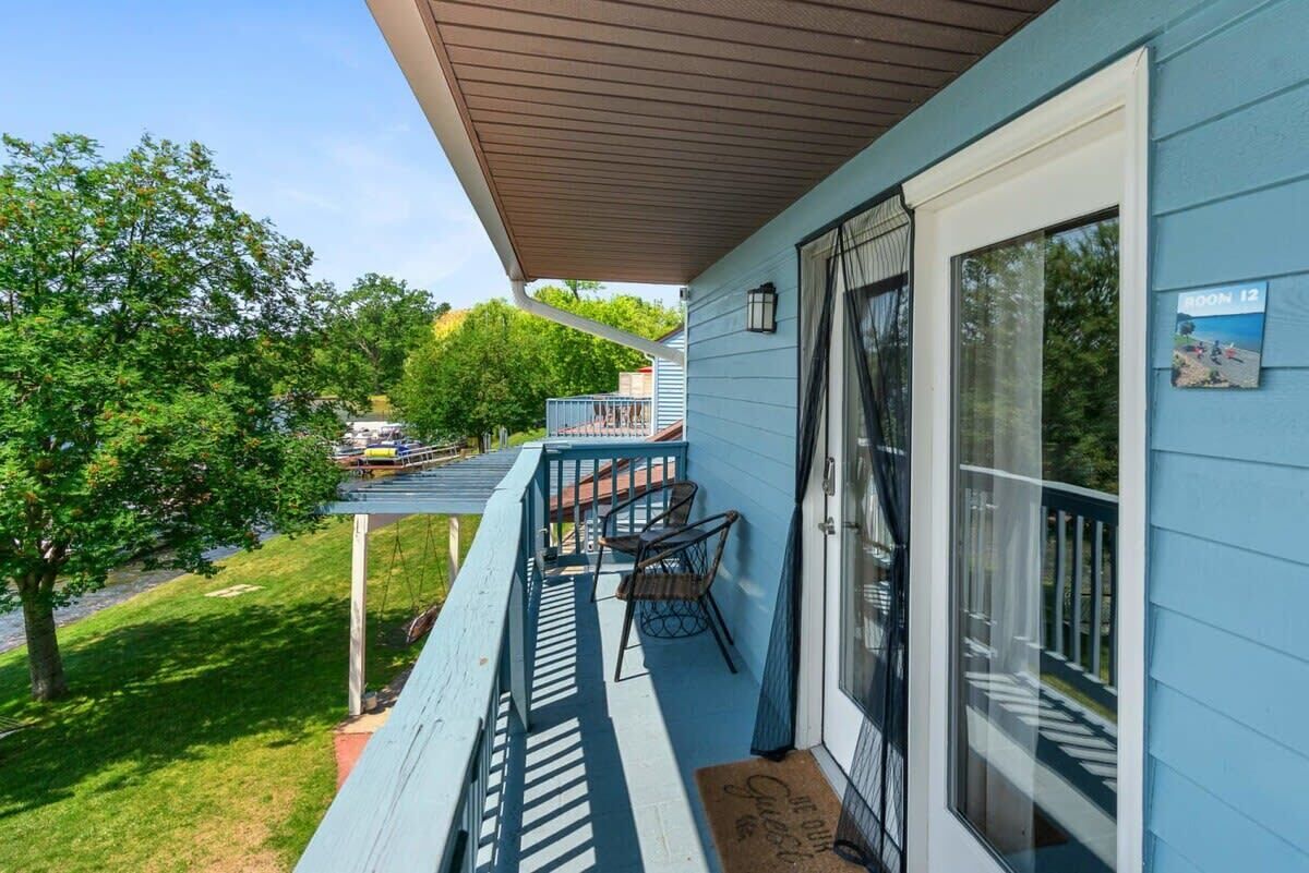 Et blåt hus med en overdækket veranda, en skydedør af glas og et lille udendørs siddeområde med stole.