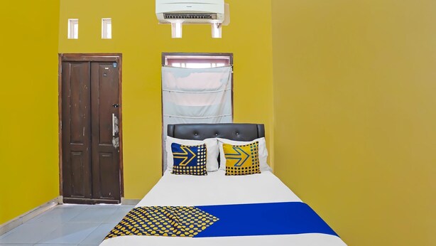 A room with a bed, a door, an air conditioning unit, and a window with a curtain. - SPOT ON 92475 Rc Homestay Syariah (Banyuwangi)