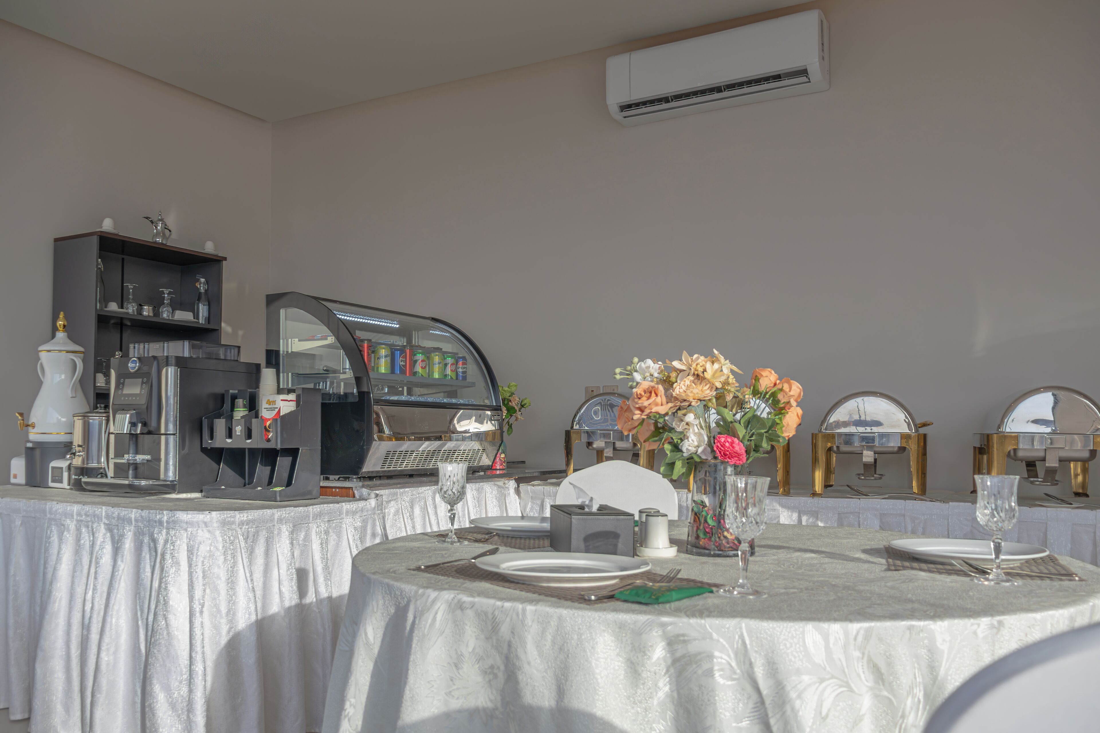 A dining area with a round table set for two, a coffee machine, and a decorative vase with flowers.