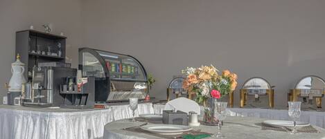 A dining area with a round table set for two, a coffee machine, and a decorative vase with flowers.